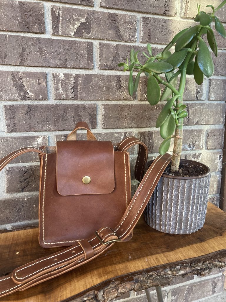 Vegetable tanned leather bag on table with brick wall and plant for scale